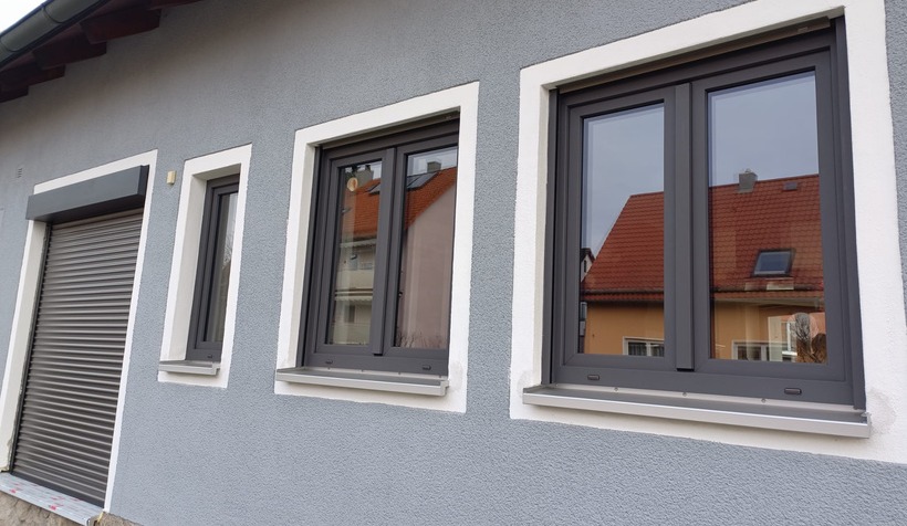 Neue anthrazitfarbene Kunststofffenster mit Rollladen an einer grauen Hausfassade